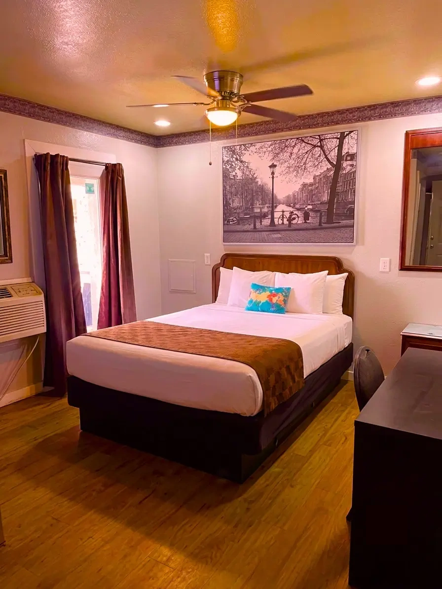 Guest room with a made bed, ceiling fan and a curtained window