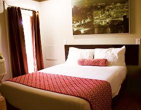 Room with a red bedspread and a framed black and white print