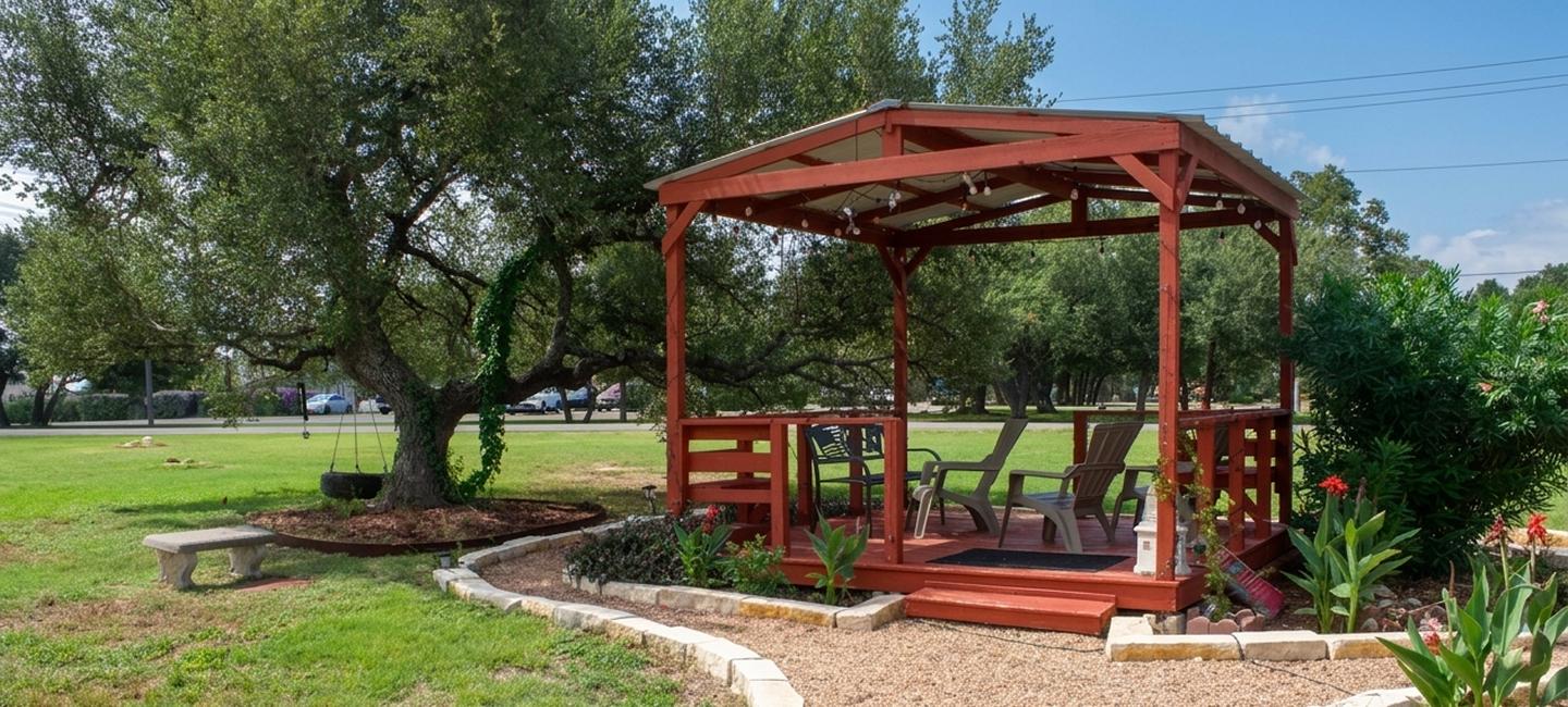 Red pergola with patio chairs and string lights on the lawn at Outpost Motel